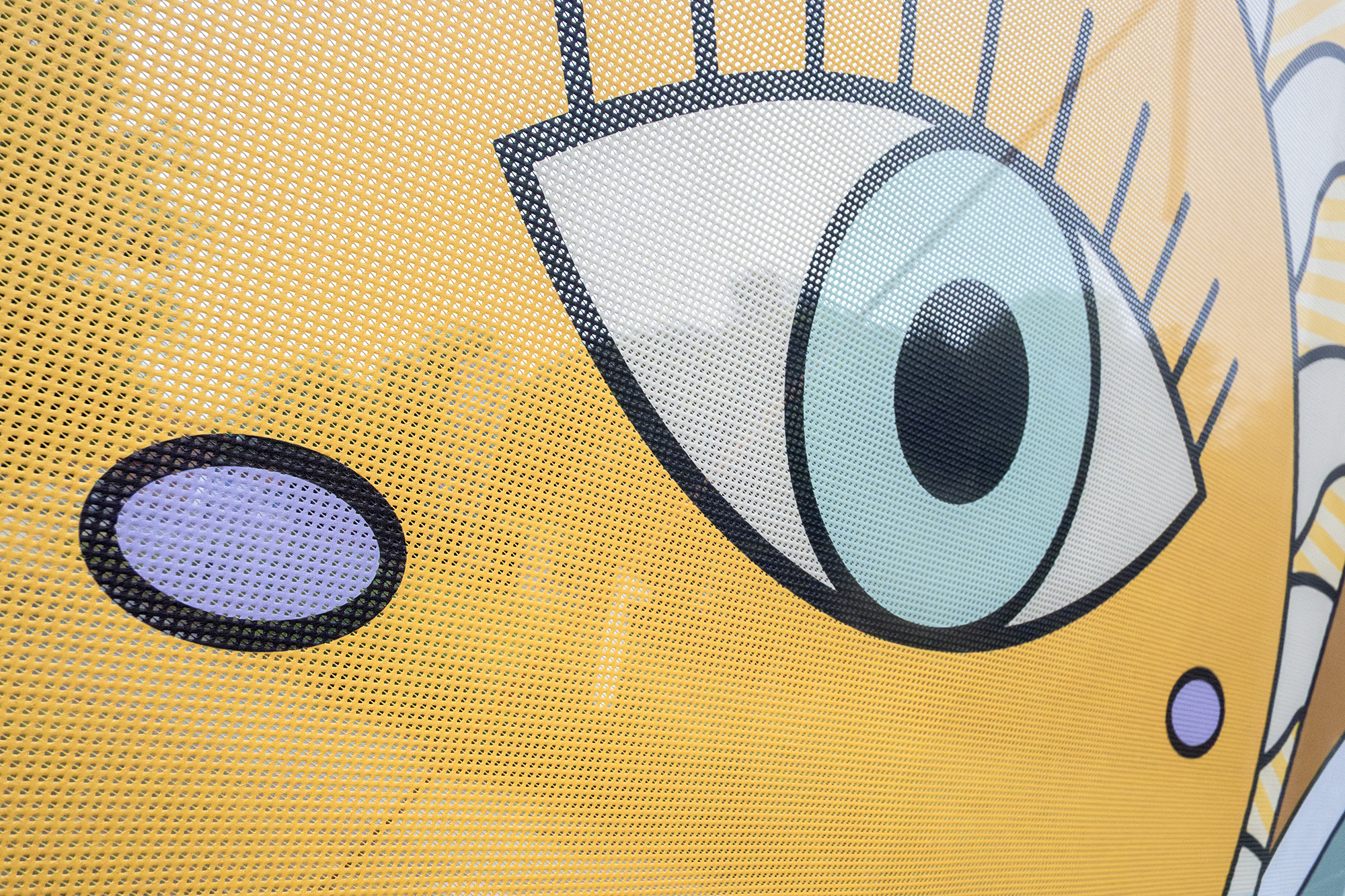 Detalle de ojo en cartel amarillo con perforaciones.
